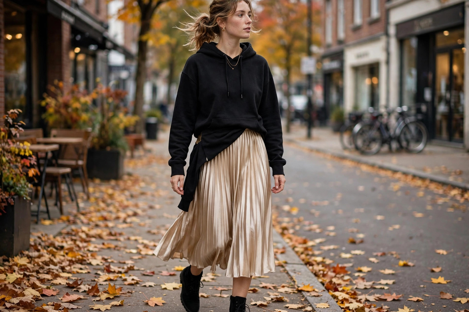 Close-up of a black hoodie paired with a pleated satin skirt and ankle boots on an autumn sidewalk